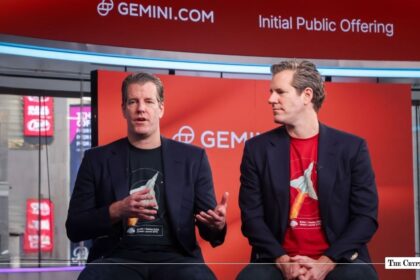 Tyler and Cameron Winklevoss seated at a Gemini Initial Public Offering setup in front of a red backdrop