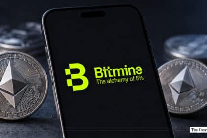 Black smartphone screen displaying the green Bitmine logo and slogan "The alchemy of 5%" surrounded by physical Ethereum coins