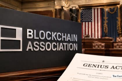 Blockchain Association sign next to a printed legislative bill titled "GENIUS ACT" with an American flag in the background