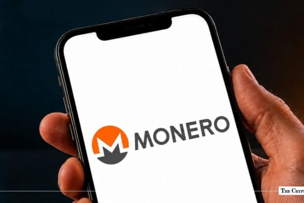 Hand holding a smartphone displaying the Monero logo and wordmark on a bright white screen
