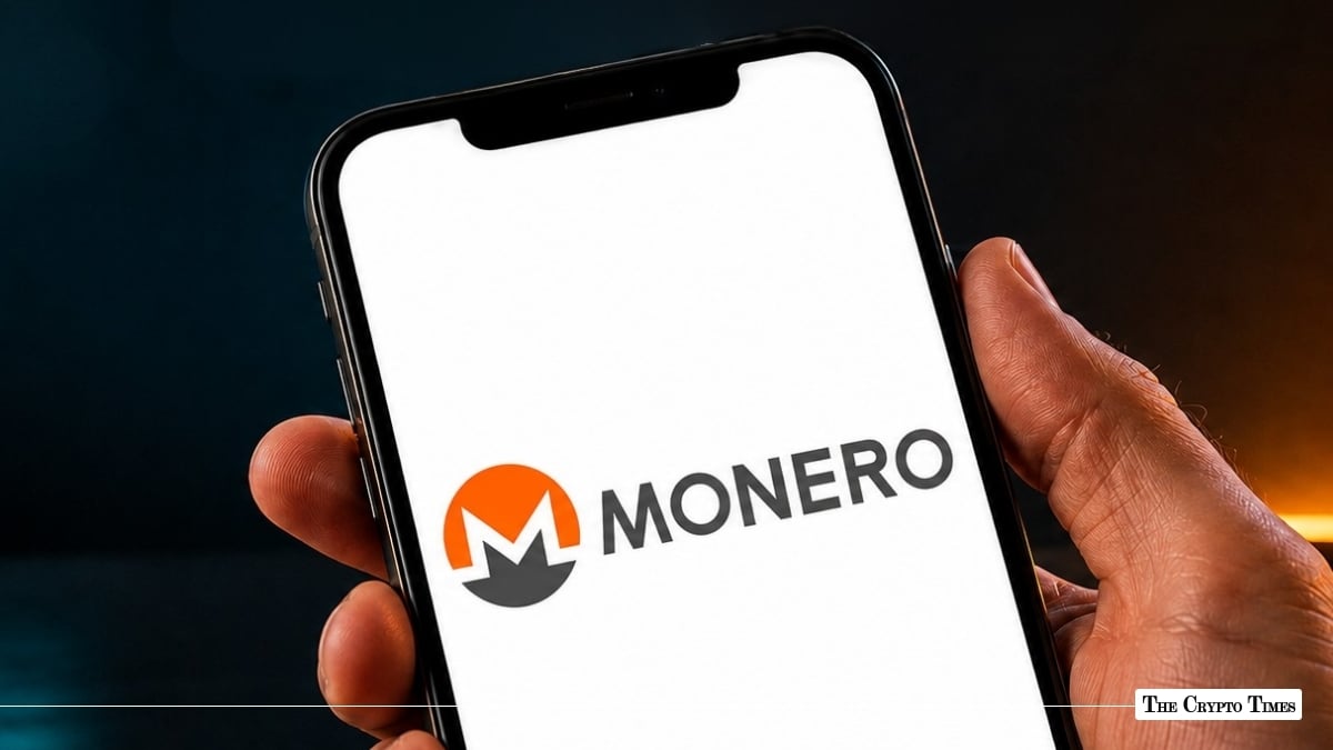 Hand holding a smartphone displaying the Monero logo and wordmark on a bright white screen