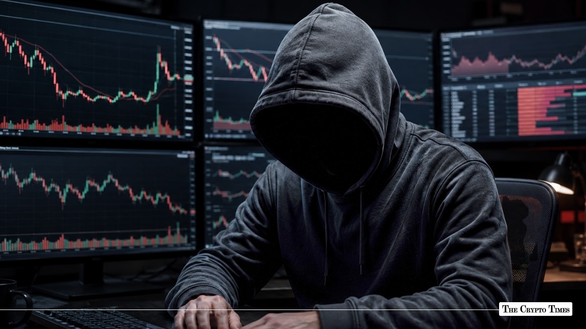 A hooded hacker sitting before multiple screens showing volatile red and green candlestick charts