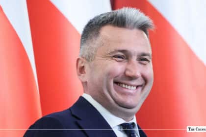 Polish Olympic Committee President Radosław Piesiewicz smiling in a suit in front of the Polish national flag