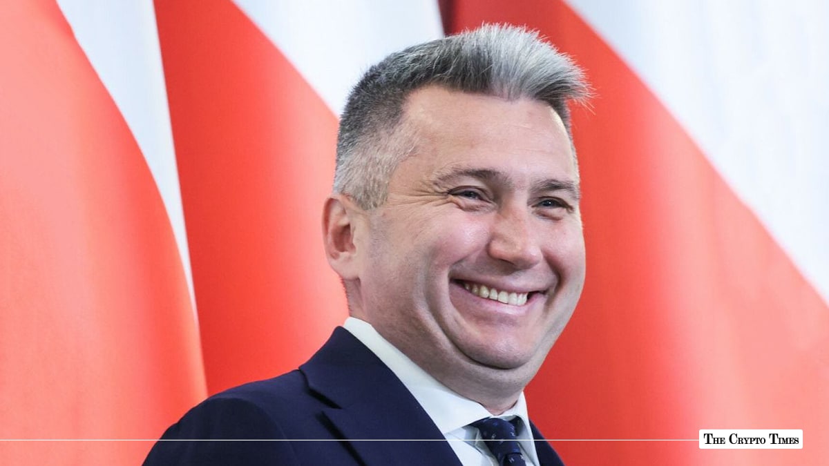 Polish Olympic Committee President Radosław Piesiewicz smiling in a suit in front of the Polish national flag