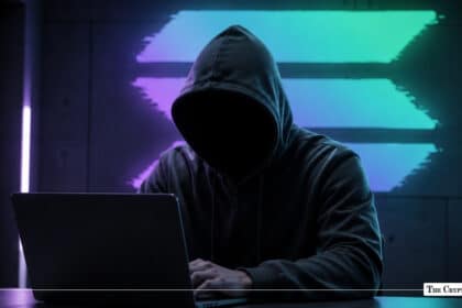 A hooded figure using a laptop in front of a glowing, multicolored Solana logo