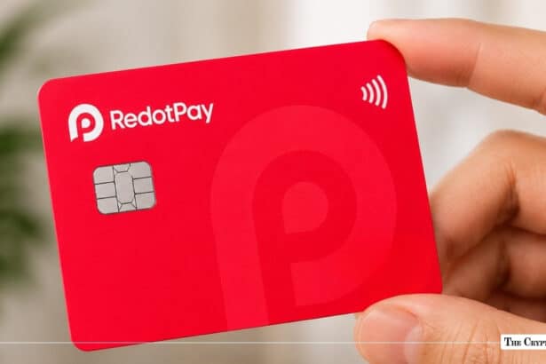 Hand holding a bright red RedotPay payment card featuring a white logo, EMV chip, and contactless payment symbol