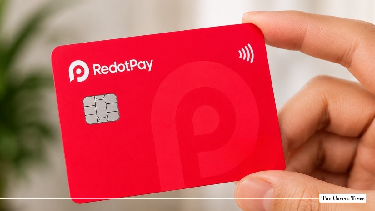 Hand holding a bright red RedotPay payment card featuring a white logo, EMV chip, and contactless payment symbol