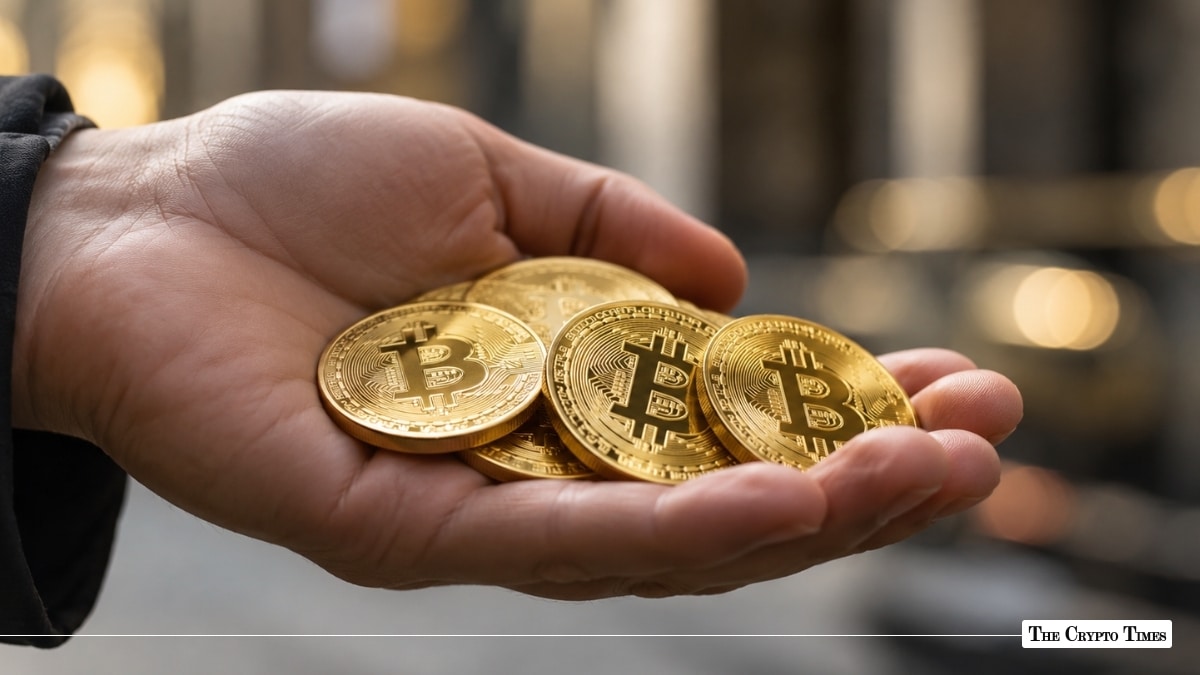 An open hand holding physical gold Bitcoin coins outdoors with a blurred background