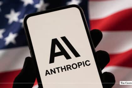 Black silhouette hand holding a smartphone displaying the Anthropic AI logo set against a blurred American flag background
