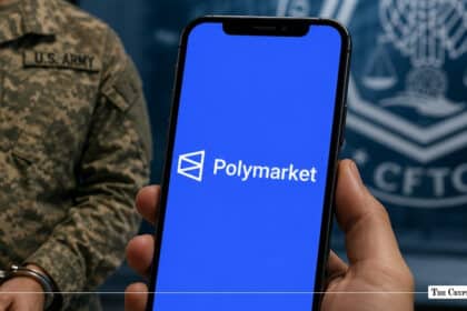 Hand holding a smartphone displaying the Polymarket logo in front of a U.S. Army soldier in handcuffs and a CFTC seal