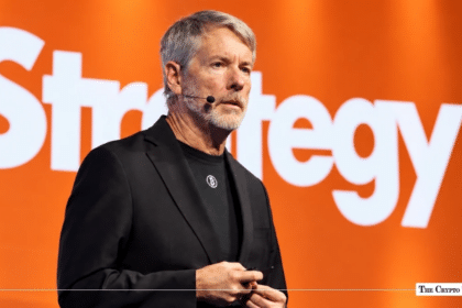Michael Saylor speaking in front of a Strategy brand backdrop with an integrated Bitcoin logo.