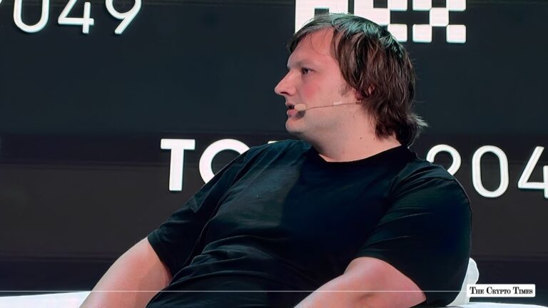Profile view of a speaker on stage wearing a black t-shirt and headset microphone at a crypto conference.