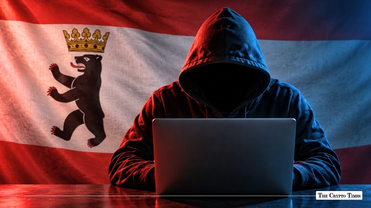 Individual in a dark hooded sweatshirt sitting in front of a laptop computer, silhouetted against an illuminated German state flag of Berlin