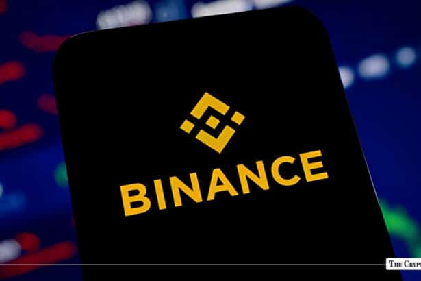 A smartphone displaying the yellow Binance logo set against a dark trading background.