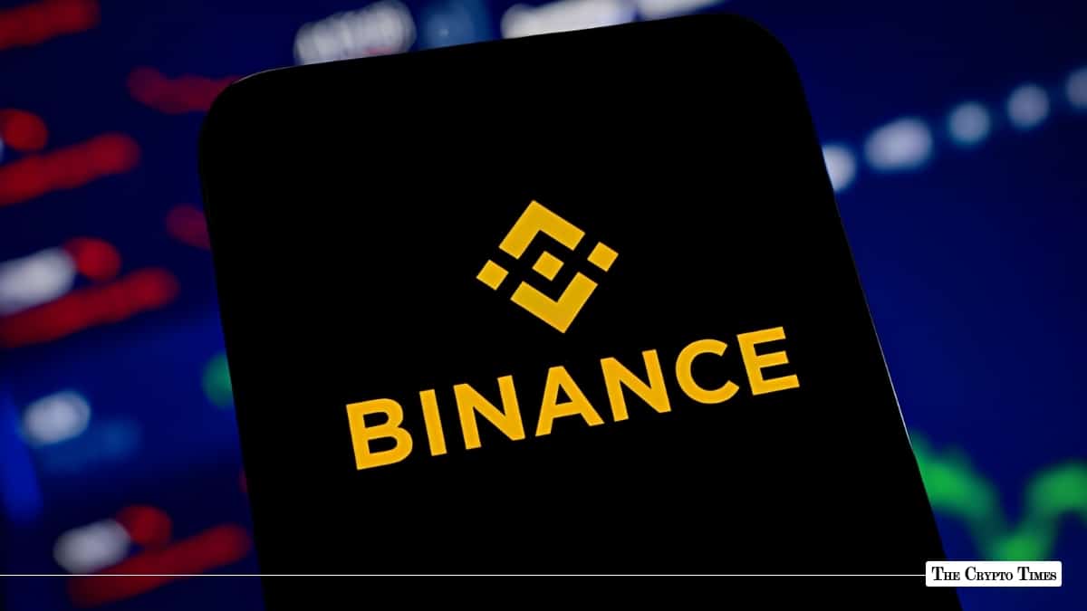 A smartphone displaying the yellow Binance logo set against a dark trading background.
