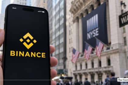 Hand holding a smartphone displaying the Binance app in front of the New York Stock Exchange