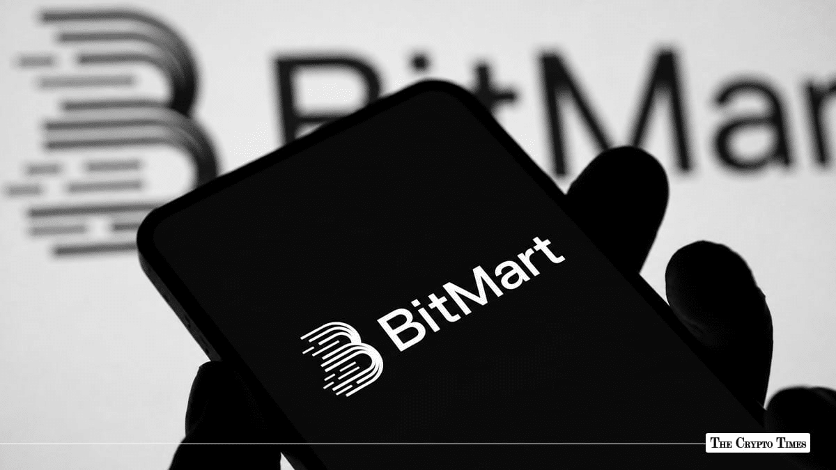 Hand holding smartphone displaying BitMart crypto exchange logo against monitor background