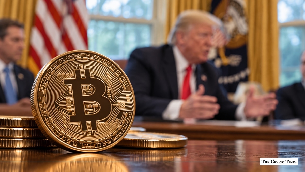 A gold Bitcoin coin on a table with Donald Trump speaking in the Oval Office in the blurred background.
