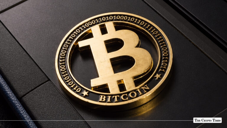 Gold-plated Bitcoin coin featuring binary code engravings on its outer ring resting on a dark, textured surface
