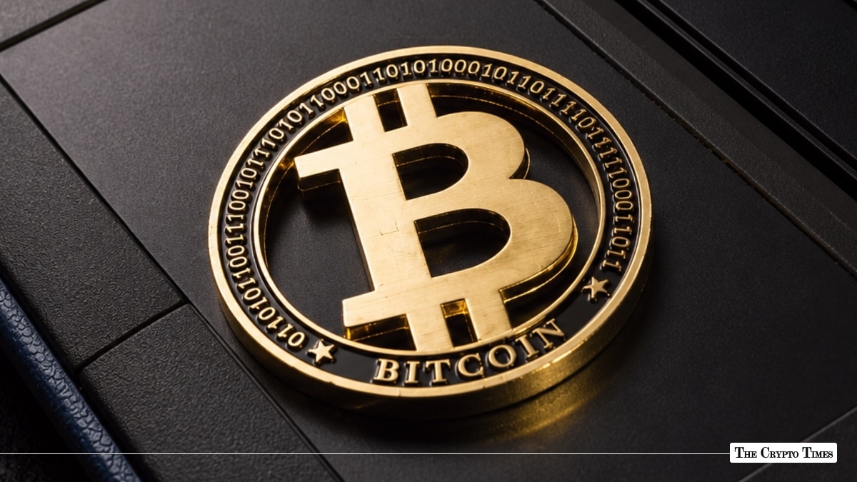 Gold-plated Bitcoin coin featuring binary code engravings on its outer ring resting on a dark, textured surface