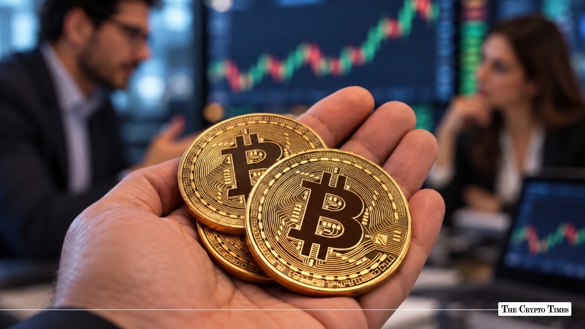 A hand holding gold Bitcoin coins with trading charts and analysts blurred in the background.