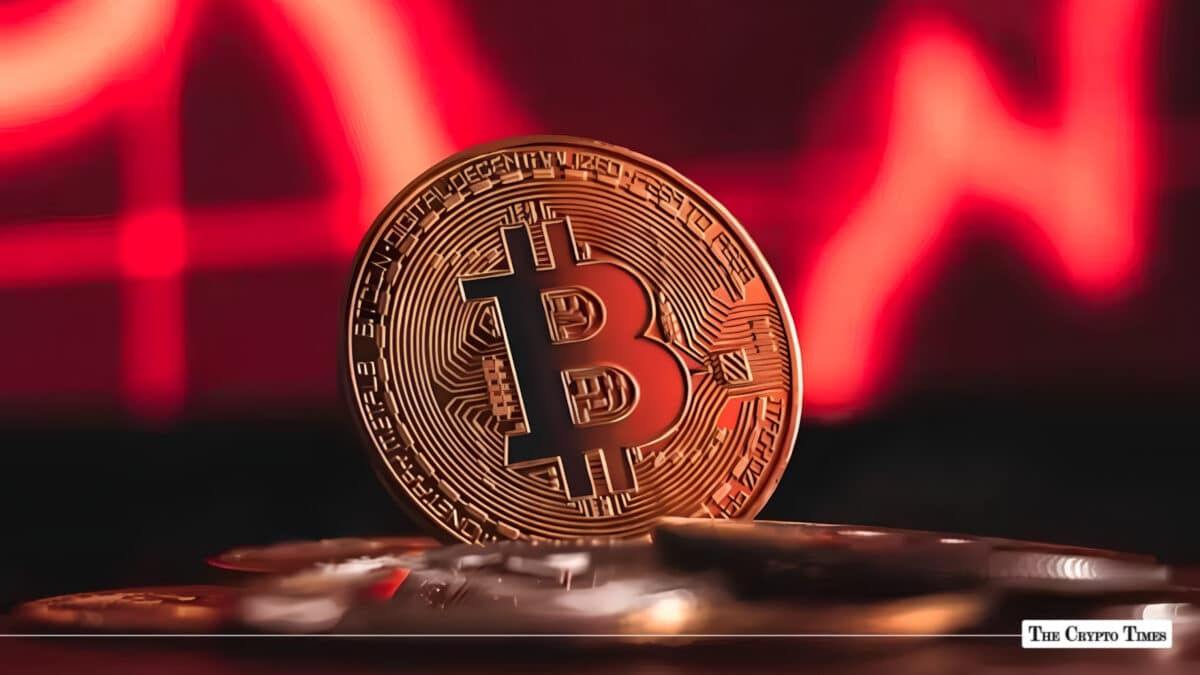 Gold Bitcoin token standing upright against a dark background illuminated with a red financial chart line