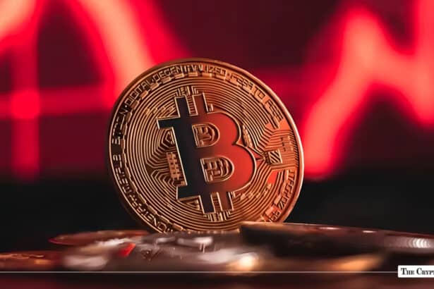 Gold Bitcoin token standing upright against a dark background illuminated with a red financial chart line