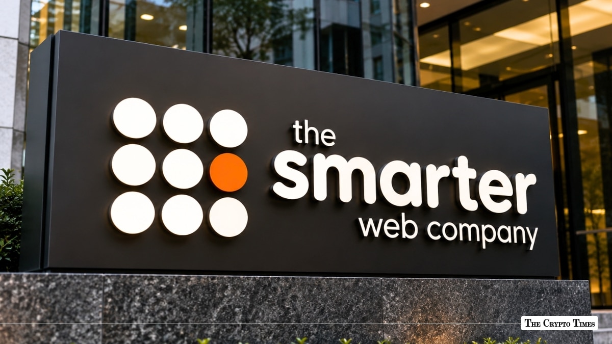 An outdoor signage board featuring the white and orange dot-grid logo and company name of "the smarter web company" mounted outside a modern office building.
