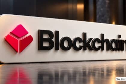 A metallic sign featuring the red geometric logo and black text of Blockchain.com set on a reflective surface.