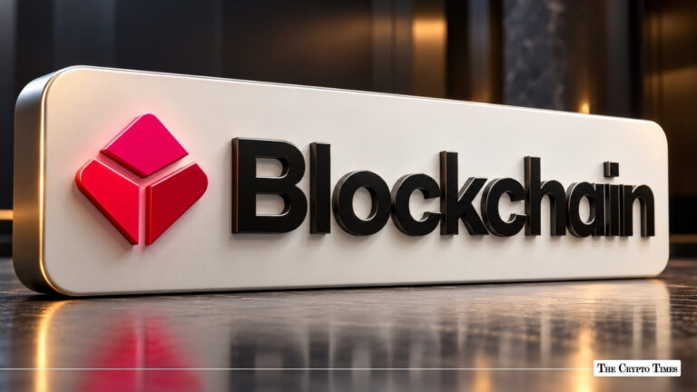 A metallic sign featuring the red geometric logo and black text of Blockchain.com set on a reflective surface.