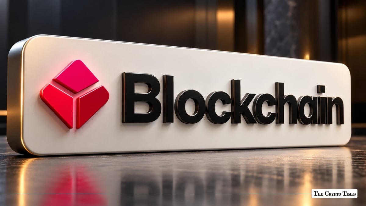 A metallic sign featuring the red geometric logo and black text of Blockchain.com set on a reflective surface.