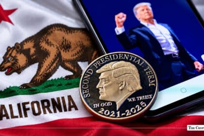 A Donald Trump commemorative coin resting on the California state flag beside a smartphone displaying Trump's image.