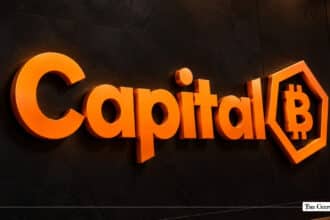 3D orange Capital B logo mounted on a dark textured wall