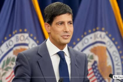 Kevin Warsh standing at a podium in front of Federal Reserve flags.