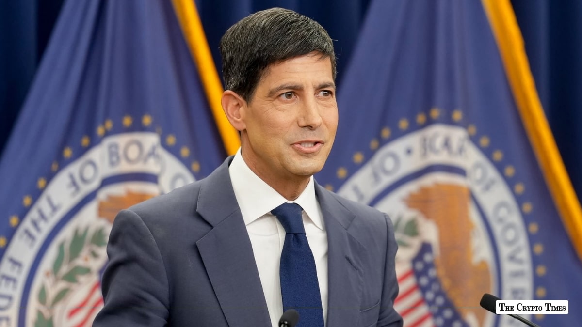 Kevin Warsh standing at a podium in front of Federal Reserve flags.