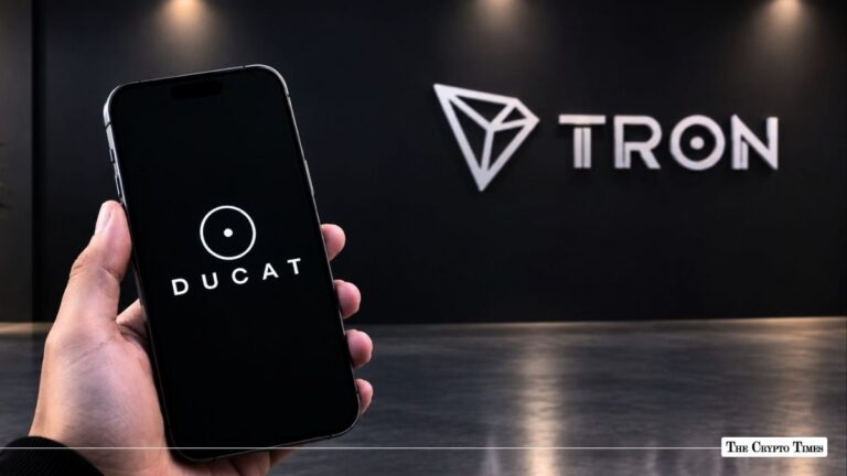 Hand holding a smartphone displaying the DUCAT logo in front of a Tron wall sign.