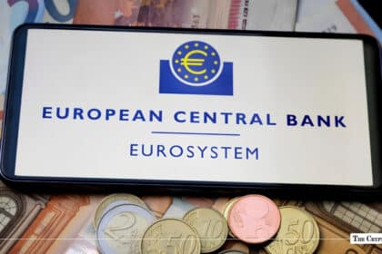 A smartphone displaying the European Central Bank Eurosystem logo placed over Euro banknotes and coins.