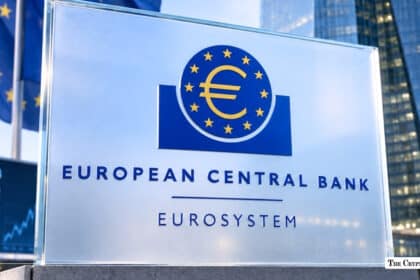 Alt Text A transparent sign displaying the European Central Bank Eurosystem logo positioned in front of a financial ticker board and modern office building.