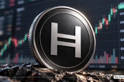 A physical Hedera (HBAR) token coin resting on a rugged surface with a financial candlestick chart showing an upward trend in the background.