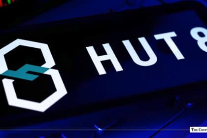 A smartphone displaying the Hut 8 logo on a screen angled over a laptop keyboard under blue lighting.