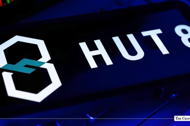 A smartphone displaying the Hut 8 logo on a screen angled over a laptop keyboard under blue lighting.