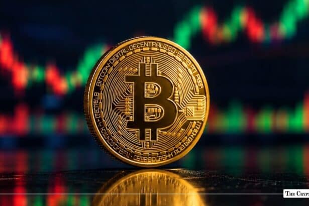 Physical gold Bitcoin (BTC) coin standing upright on a reflective dark surface in front of a red and green trading chart background.