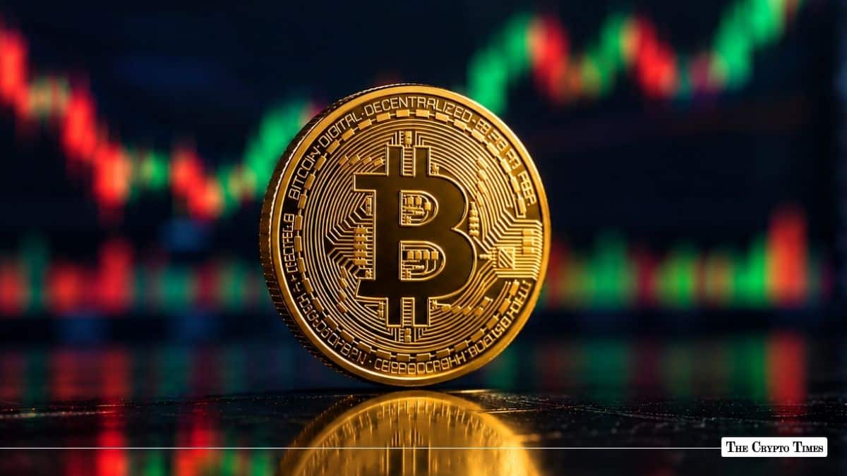 Physical gold Bitcoin (BTC) coin standing upright on a reflective dark surface in front of a red and green trading chart background.