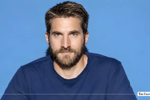 Studio headshot of a man with short brown hair and a beard against a blue background.