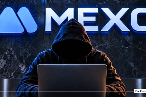 A hooded figure working on a laptop in front of an illuminated MEXC logo on a dark wall.