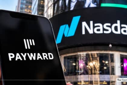 Hand holding a smartphone displaying the Payward logo set against the illuminated Nasdaq outdoor building sign in Times Square