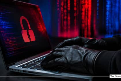 Gloved hands typing on a laptop displaying a cracked red padlock icon against a background of digital code matrix lines