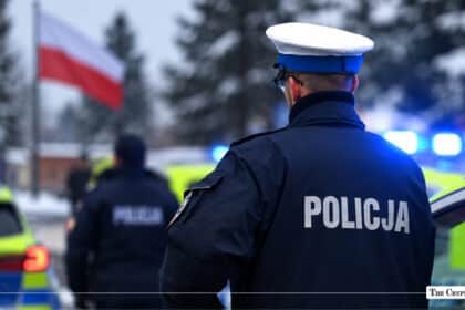 Polish police officer in uniform standing near police vehicles with the Polish flag in the background