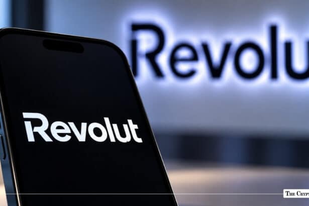Smartphone displaying the Revolut app logo against a dark background with an illuminated Revolut wall sign behind it.