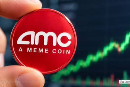 Hand holding a physical red coin stamped with "AMC A MEME COIN" against a green upward-trending candlestick chart